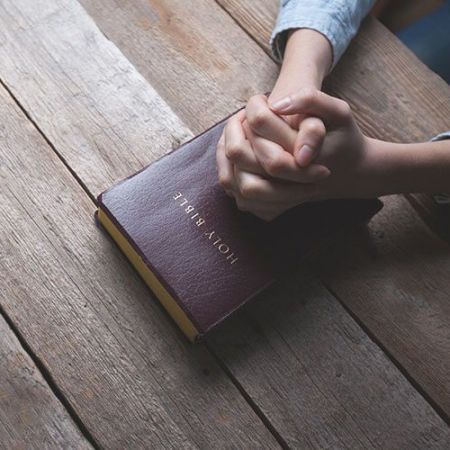 Hands in prayer resting on Bible